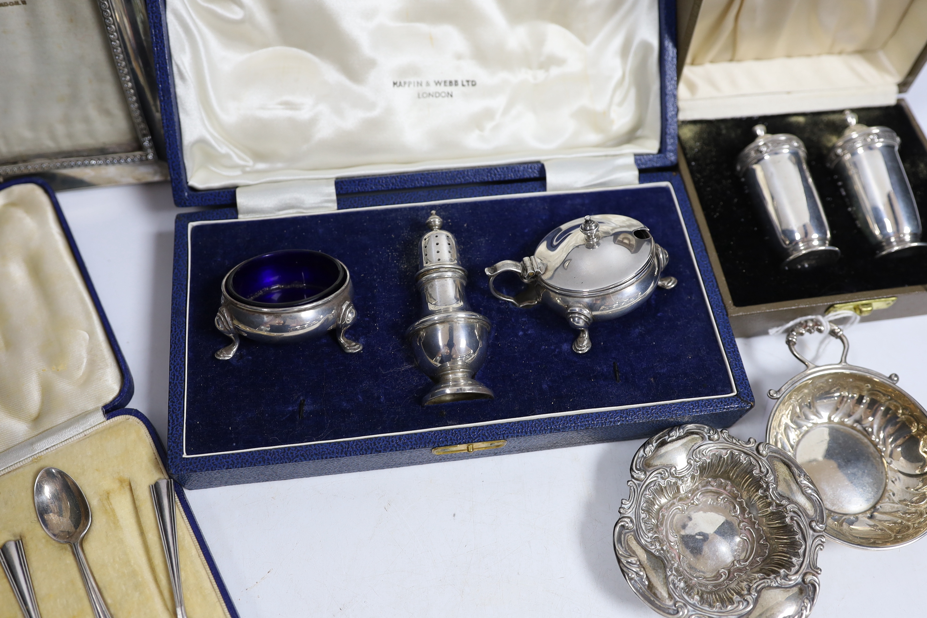 An Elizabeth II cased silver three piece condiment set by Mappin & Webb, a cased pair of Irish silver pepperettes, a cased set of six silver coffee spoons, two silver dishes and a silver mounted photograph frame.